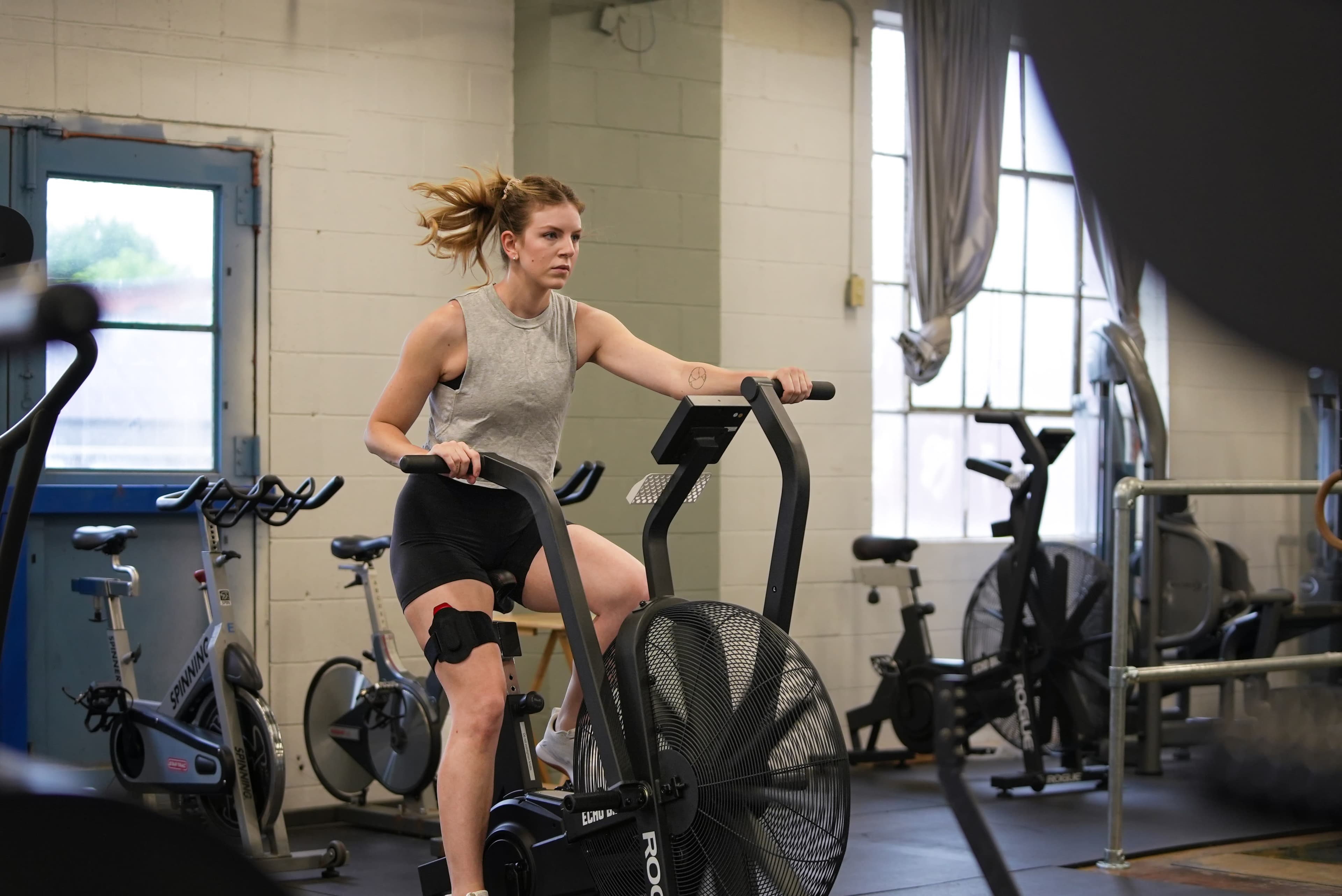 A woman training outdoors, lifting her knee with focus.